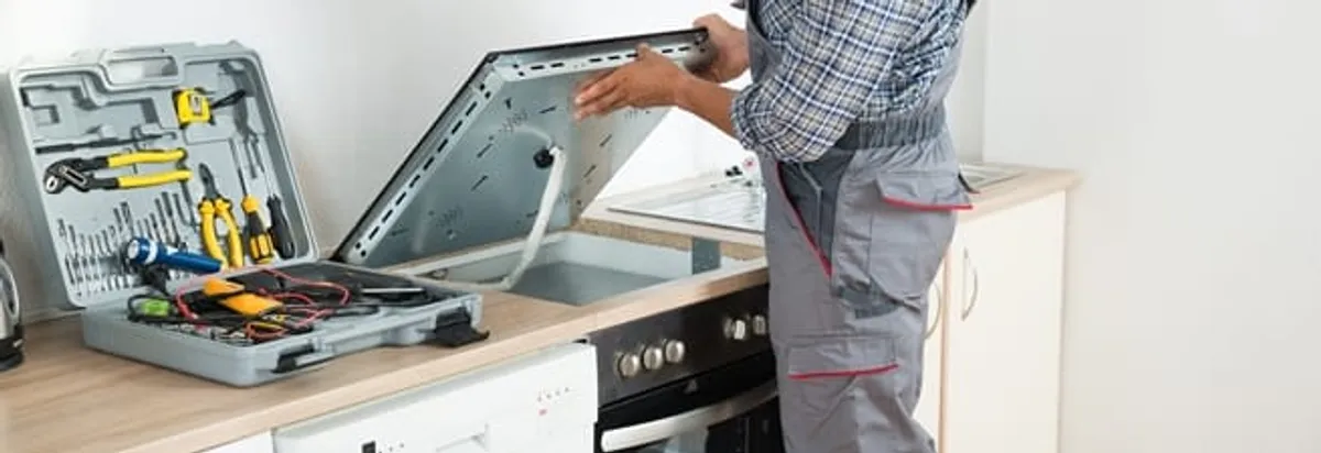 Cooktop repair technician lifting a built-in stovetop for service in Huntsville, AL