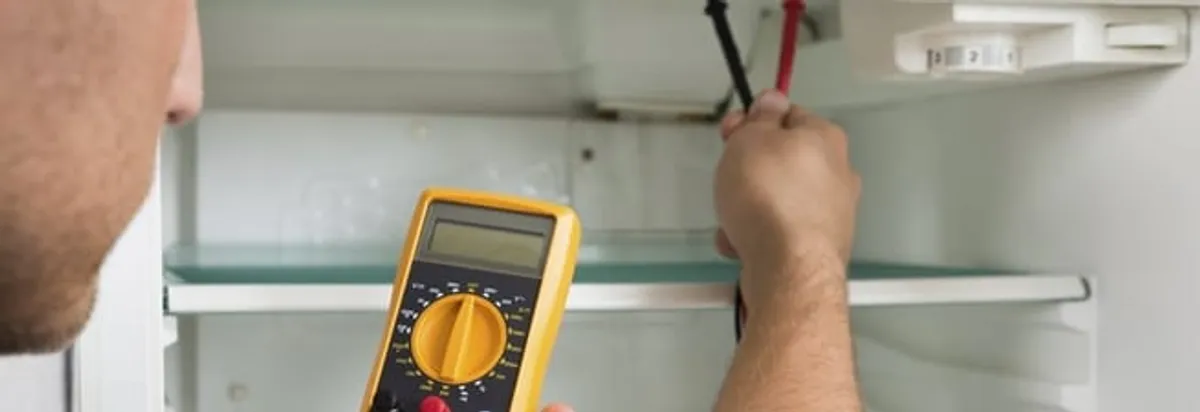 Refrigerator repair technician testing electrical components with a multimeter in Huntsville, AL